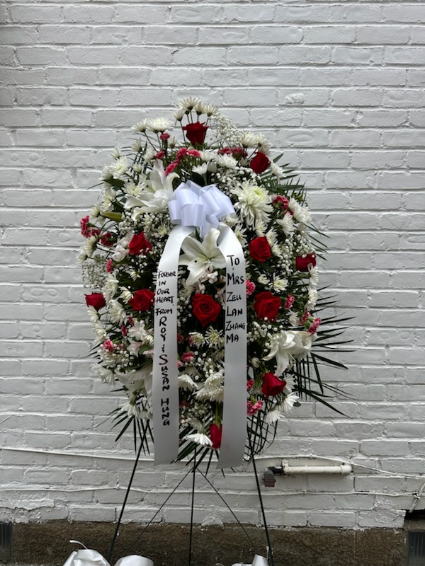 A funeral arrangement with mostly white and red flowers with a ribbon on the middle
